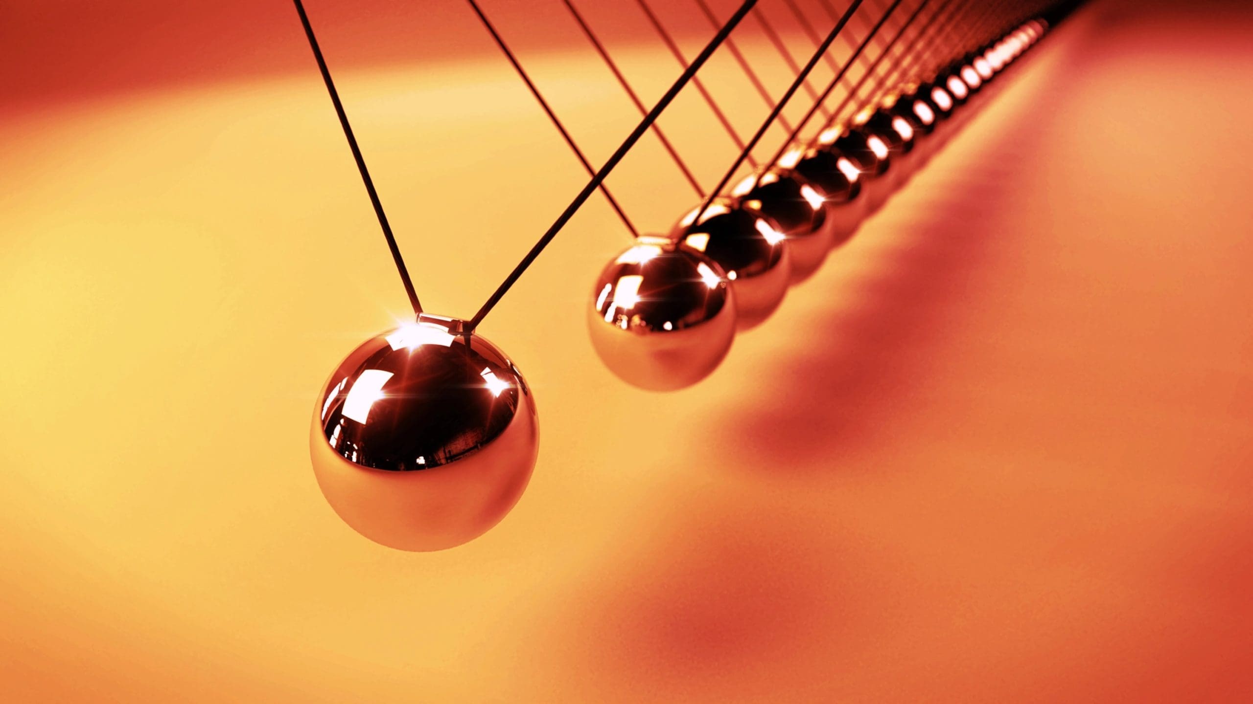 Close-up of a Newton’s cradle with metallic balls suspended in motion against an orange background.