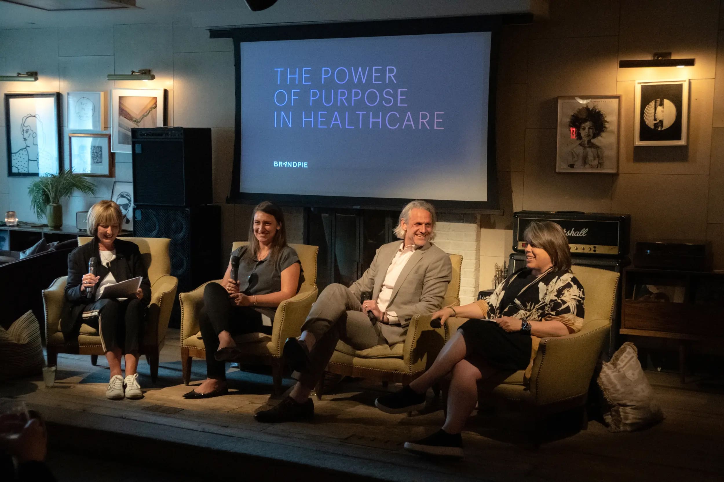 Four speakers sit on stage with microphones during a panel discussion titled “The Power of Purpose in Healthcare,” hosted by Brandpie, with framed art and warm lighting in the background.