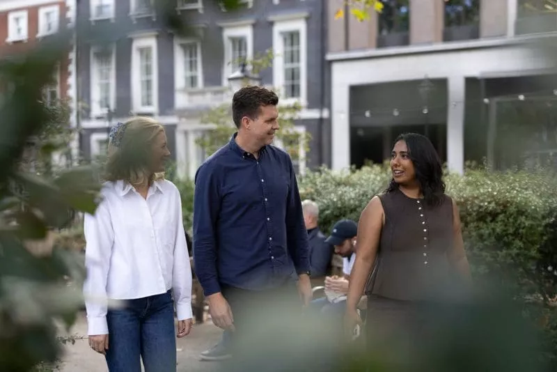 Three people walking and talking outdoors in an urban park setting.