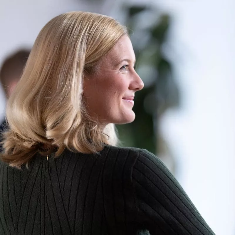 Person smiling in profile view, wearing a dark ribbed top with a blurred background.