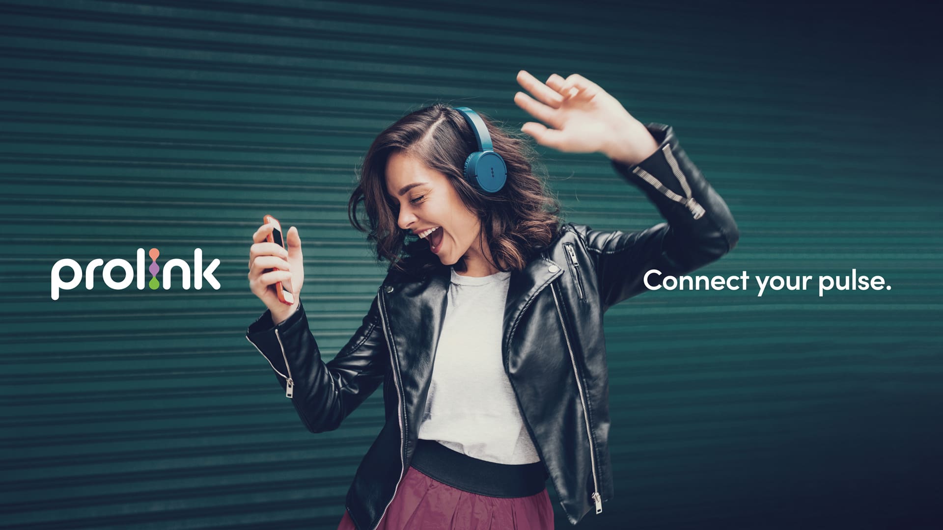 Young woman wearing blue over-ear headphones dances while holding a smartphone, smiling with one arm raised. The Prolink logo appears on the left and the tagline “Connect your pulse.” on the right against a teal textured background.