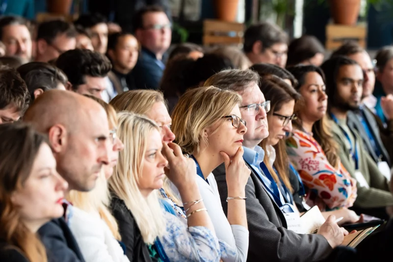 Audience members seated closely together at Anthropy, Eden Project, listening attentively to a speaker, many wearing event lanyards and looking focused.