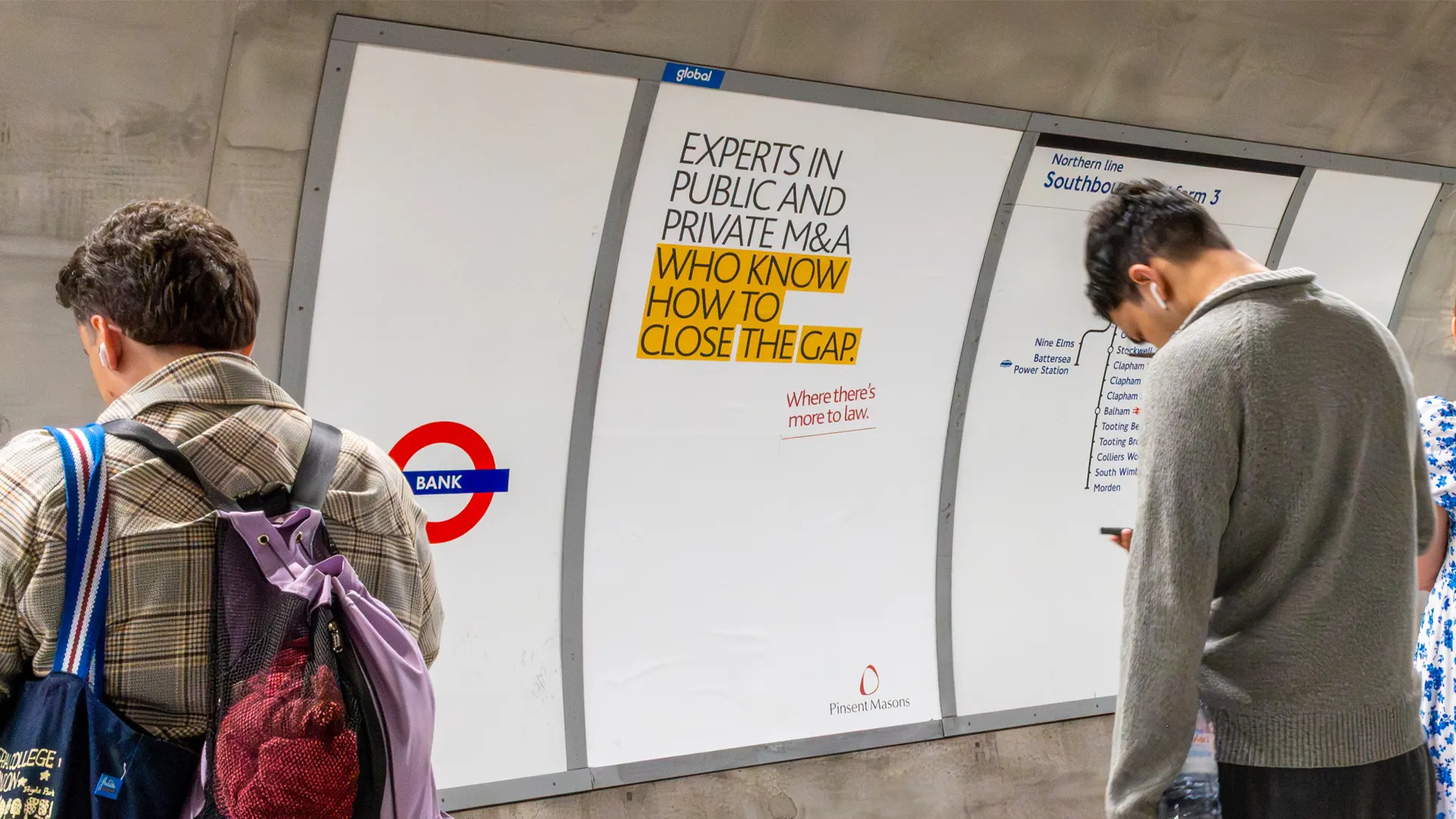 Commuters wait at Bank station beside a Pinsent Masons poster with yellow-highlighted text reading “Experts in public and private M&A who know how to close the gap.”