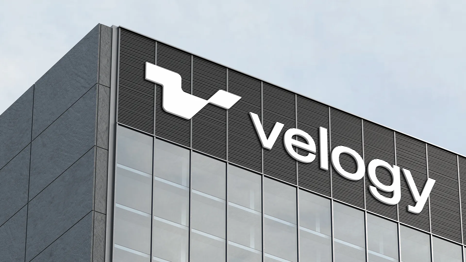 White Velogy symbol and wordmark mounted high on the dark façade of a modern industrial building.