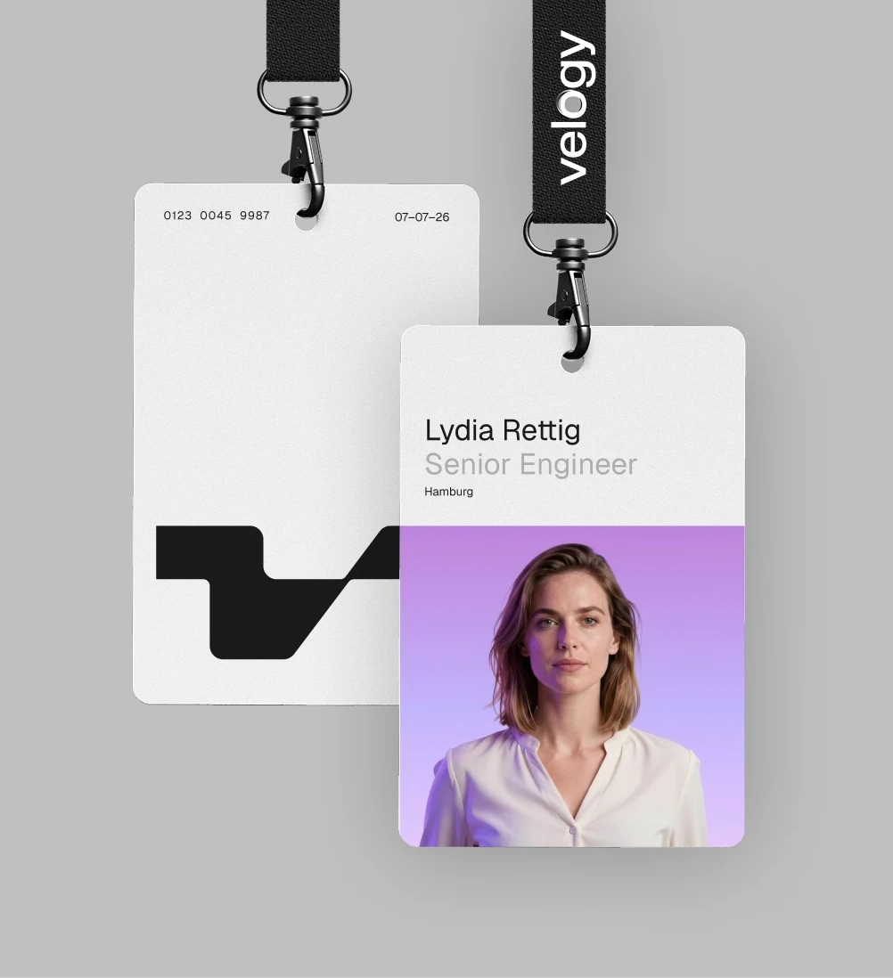 Front and back of a Velogy employee ID badge on black branded lanyards, with a portrait and bold black logo.