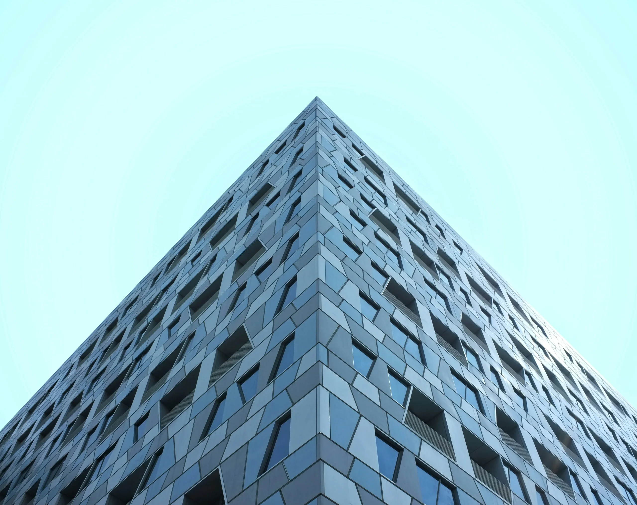 Low-angle view of a modern glass and steel building rising into a clear blue sky.